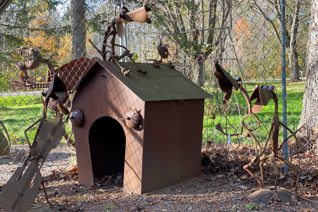 a dog house and several small dogs made of scap metal sit outside