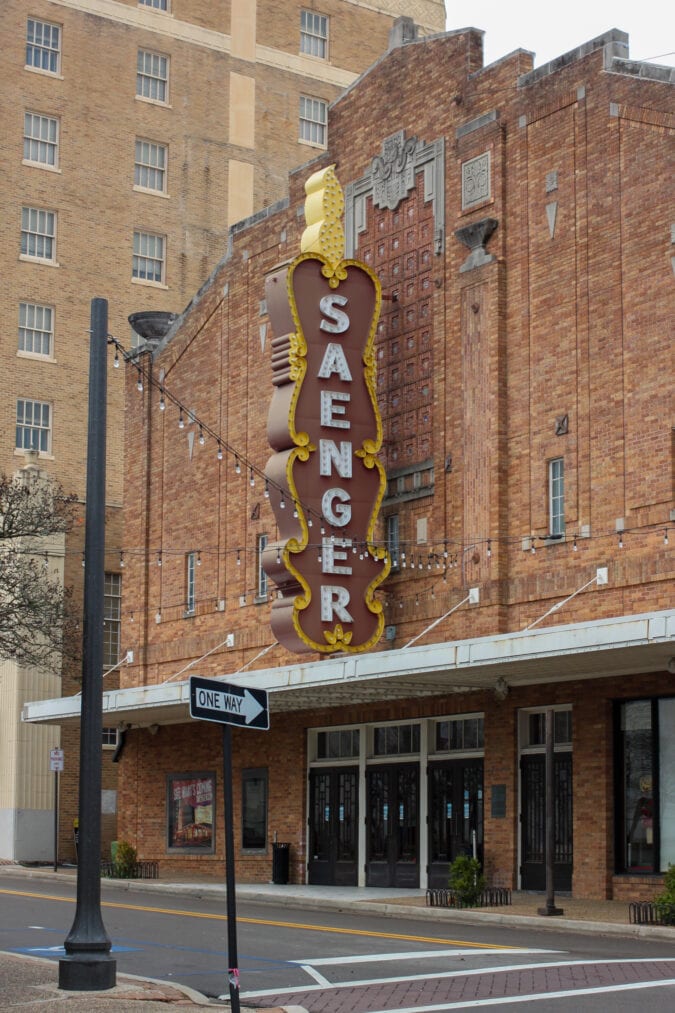 the outside of the art deco red brick building with a vertical marquee sign that says "saenger"
