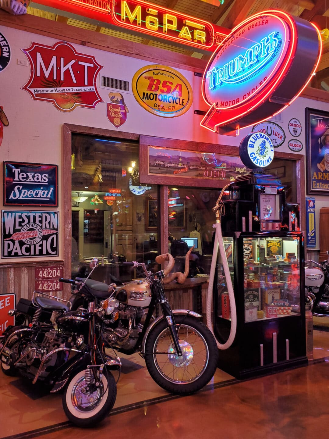 Triumph motorcycles and a vintage gas pump in a room filled with neon signs