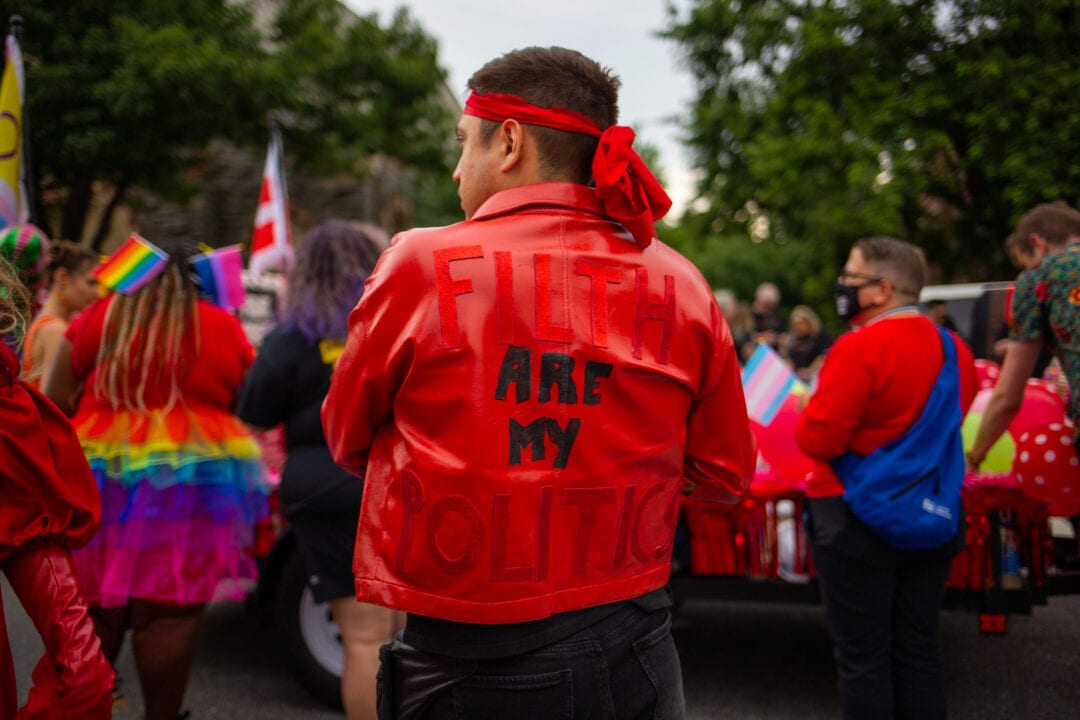 a person wears a red leather jacket with the words "filth are my politics" adhered to the back