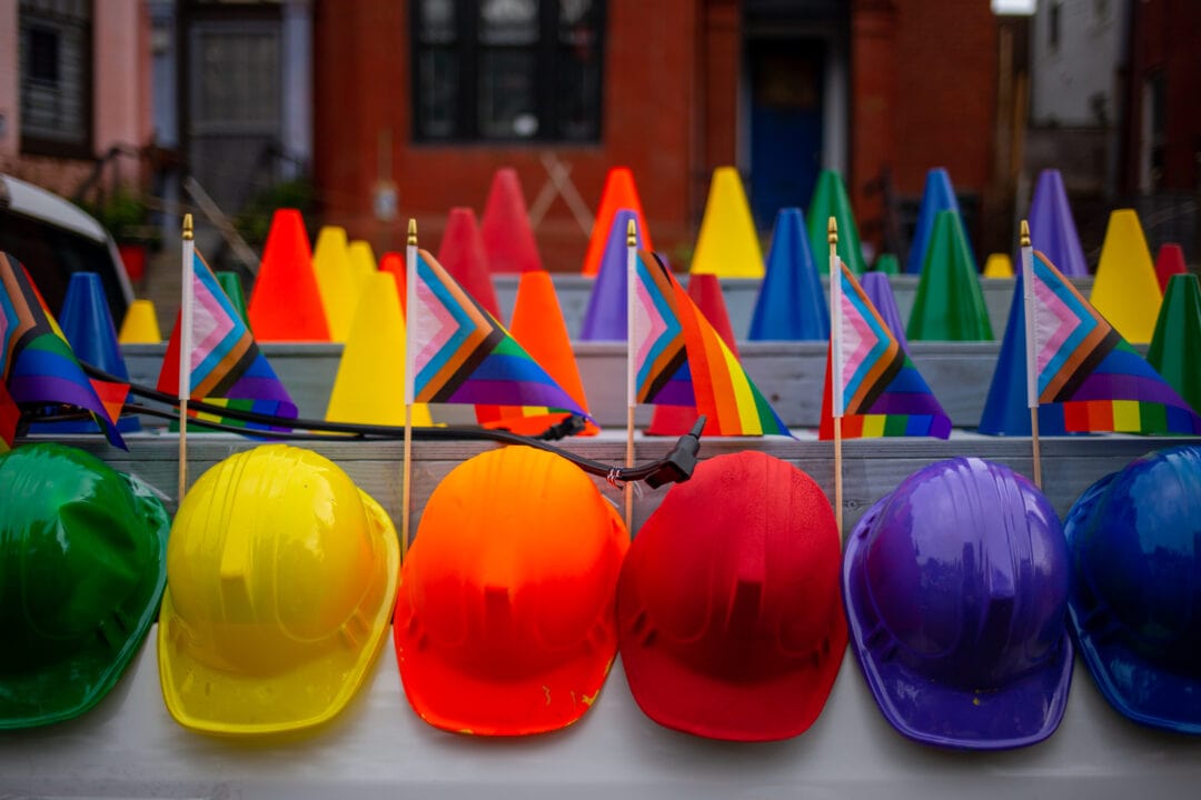 a line of pride flags and construction hats arranged in rainbow order