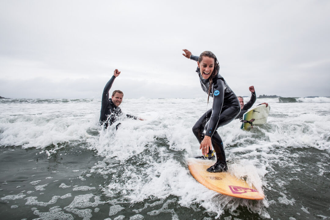 A woman surfing a wave with two smiling people in the background
