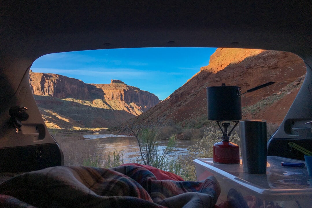 a view of red rocks and water from the back of an open hatchback door