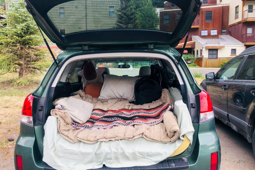 a green hatchback car with its trunk open with a bed setup in the back
