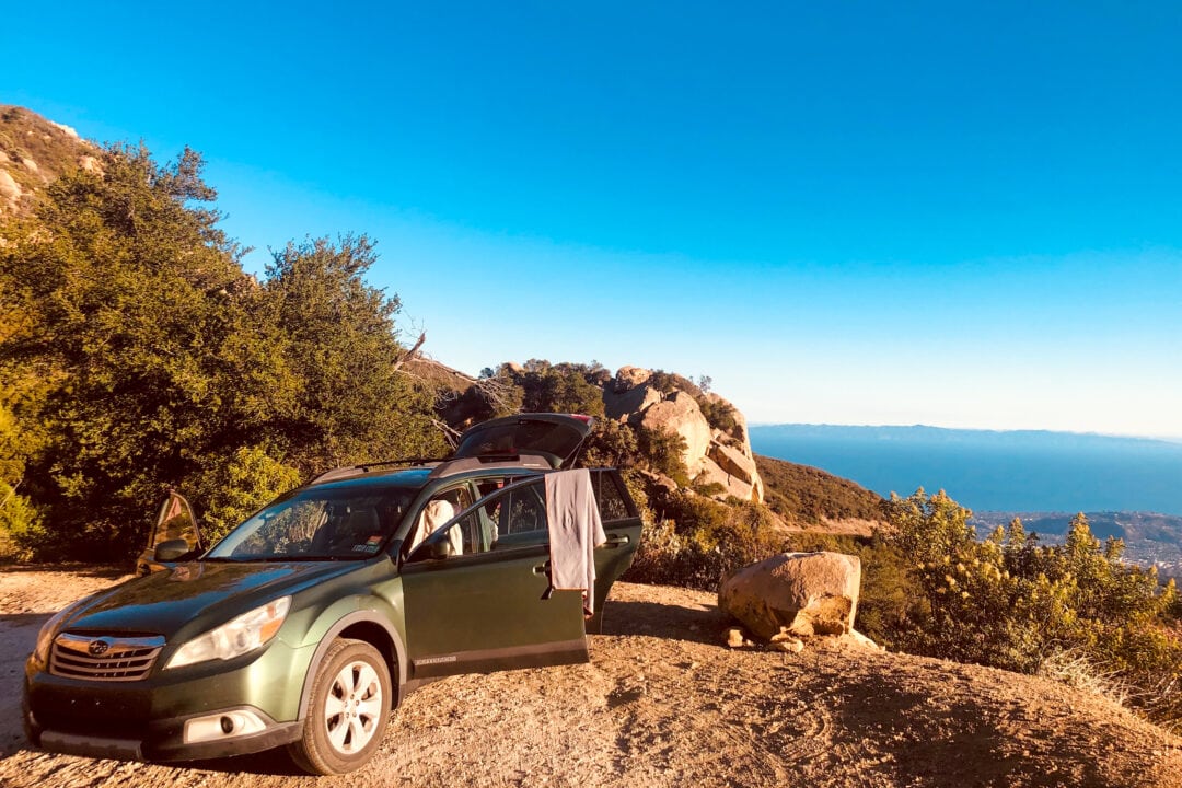 A green hatchback with open doors is parked on a scenic mountain view
