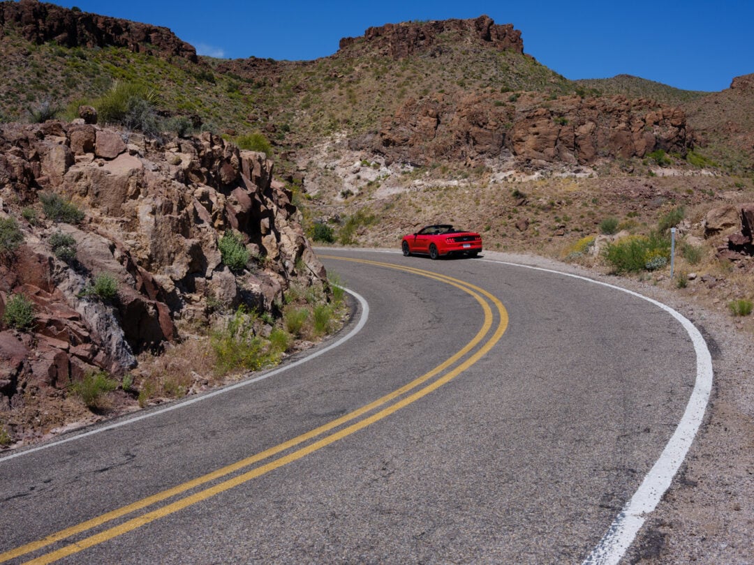 a red convertible drives on a winding road through a desert landscape under clear blue skies