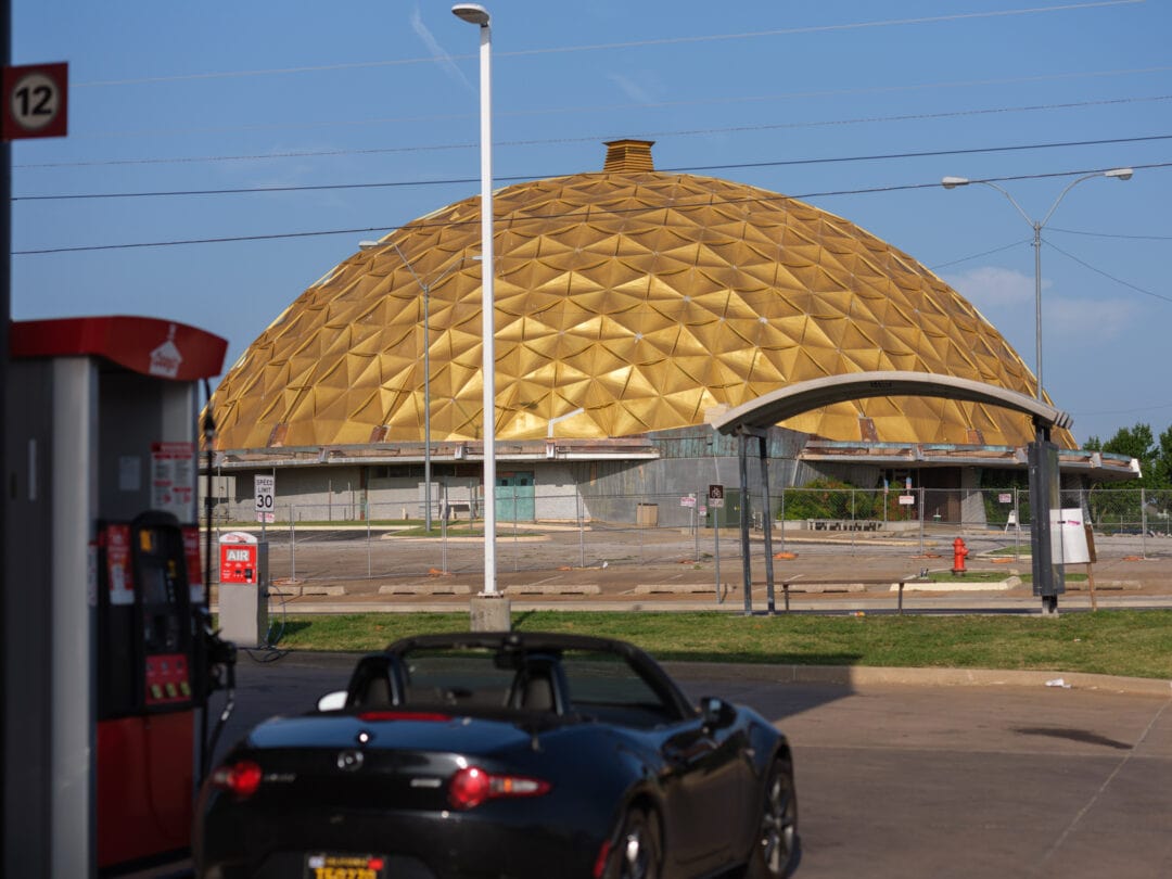 a black convertible is parked at a gas pump in front of a gold-domed building