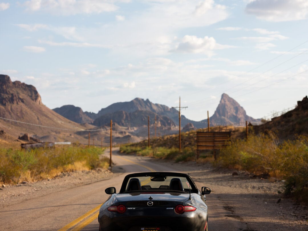 a black roadster convertible is parked on a road surrounded by mountains