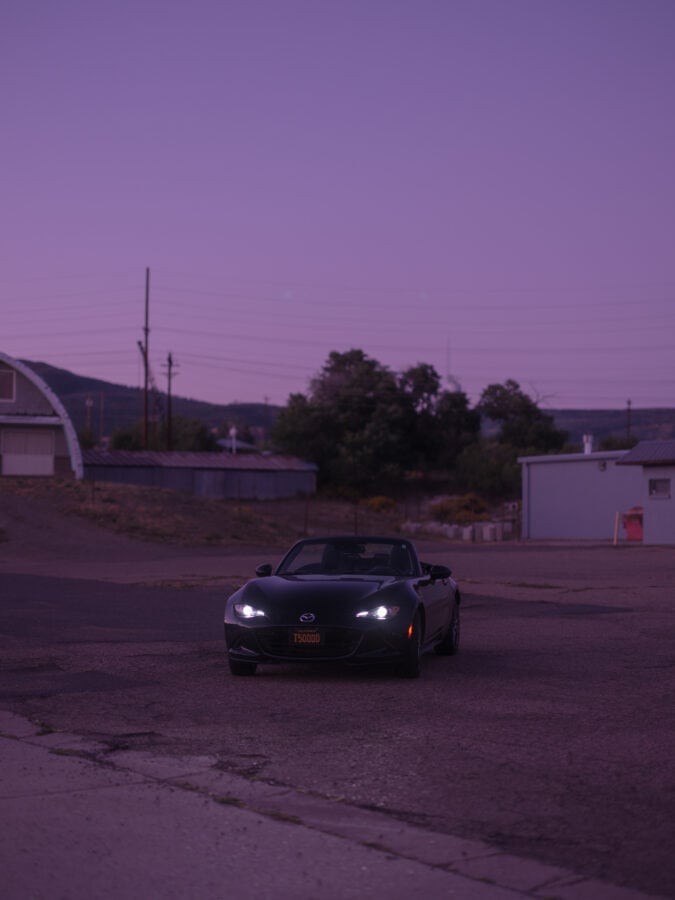 a convertible is parked in a lot at night with its headlights turned on under a purple sky