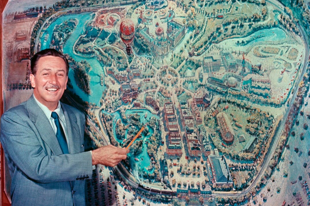 walt disney stands in front of and points to a map of disneyland