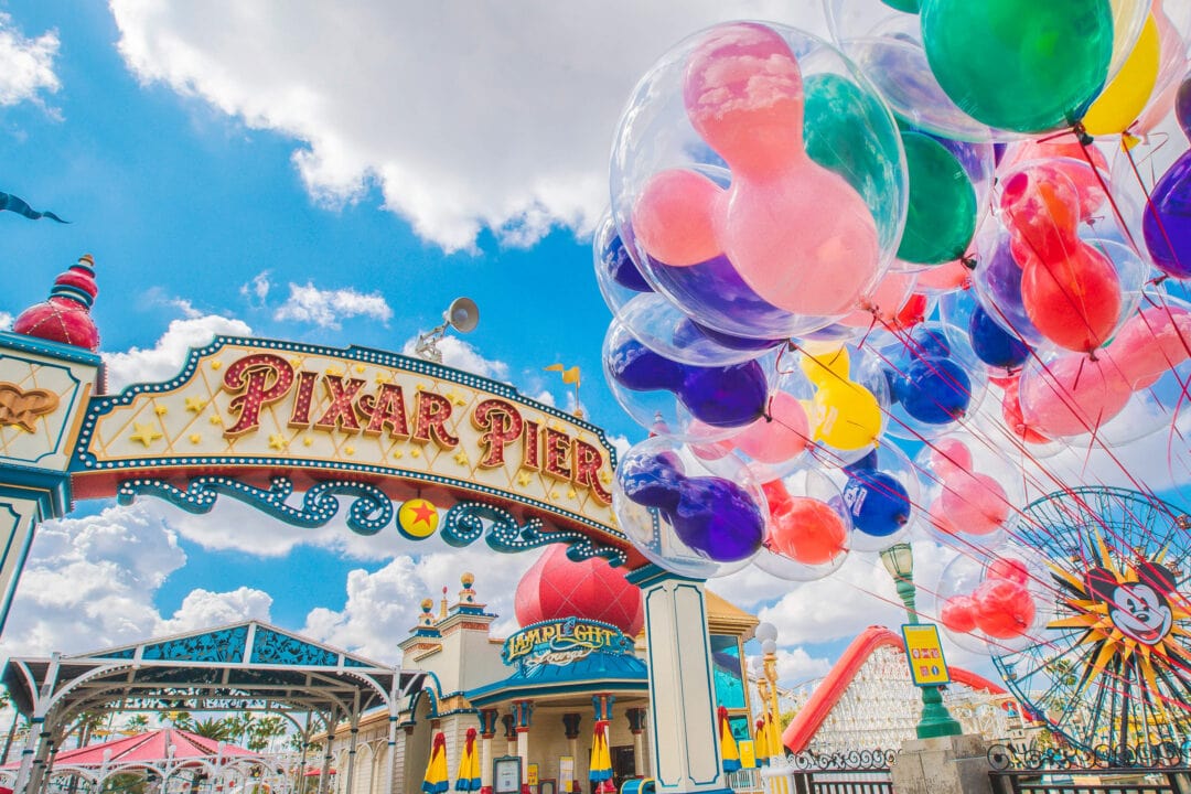 an outdoor pier featuring a ferris wheel and a bunch of colorful mickey-mouse-shaped balloons