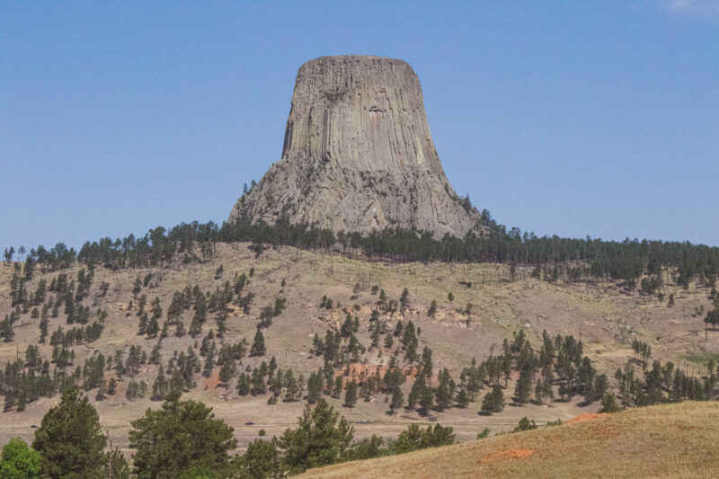 a large gray rock formation rises from the landscape in front of a clear blue sky