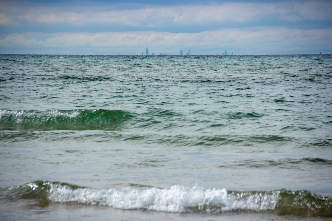the chicago skyline is visible on the horizon over the lake as waves crash on the shore