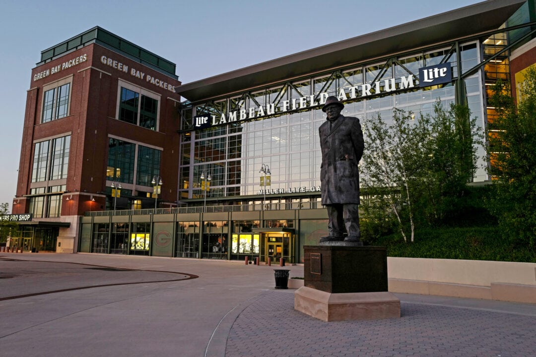 a bronze statue of Vince Lombardi stands watch over Lambeau Field at dusk