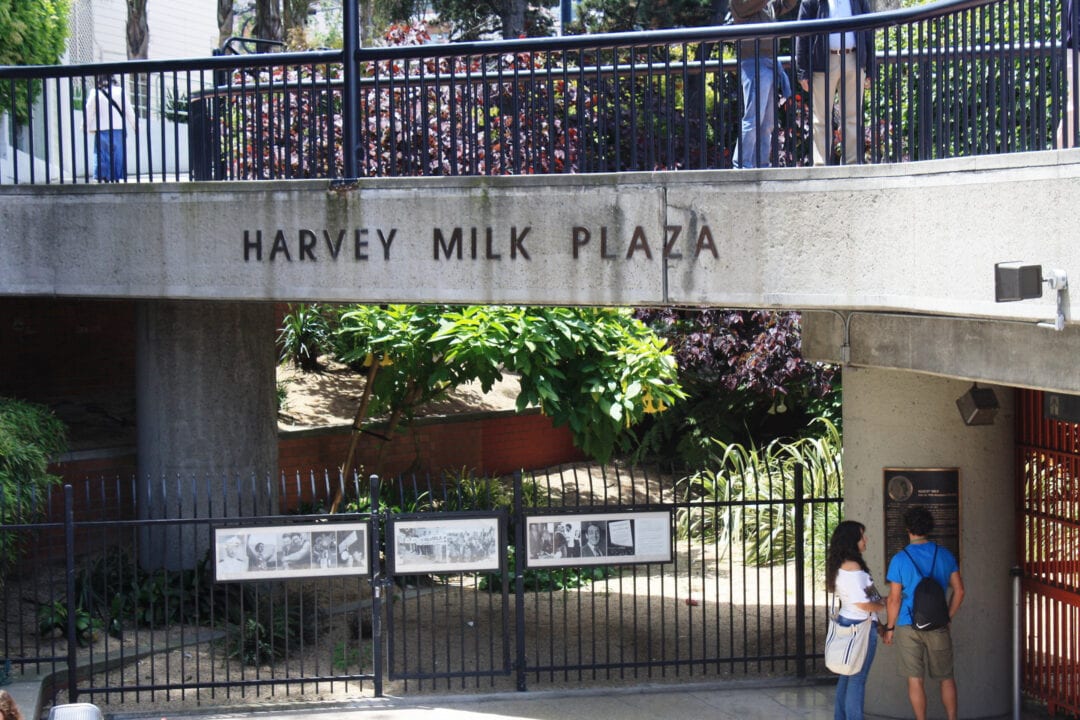 two people stand under a concrete overpass that says harvey milk plaza