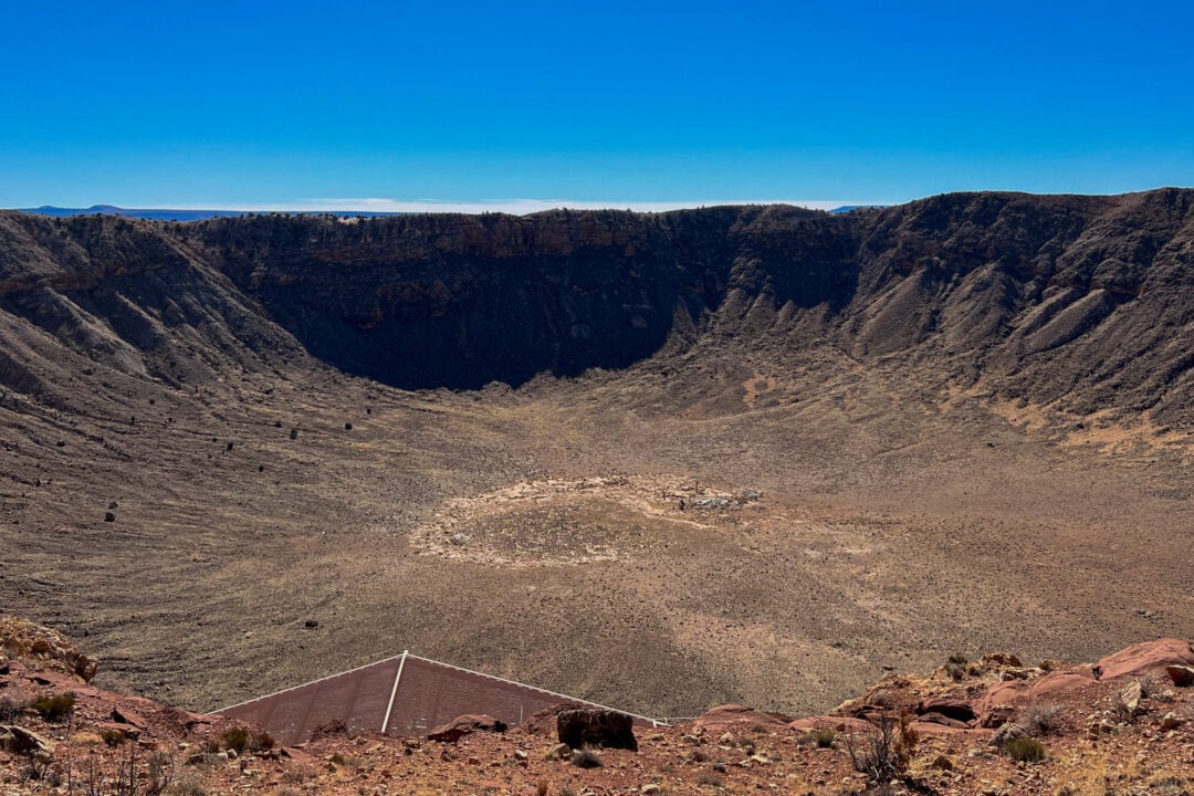 a large crater in the dirt made by a meteor under a clear blue sky
