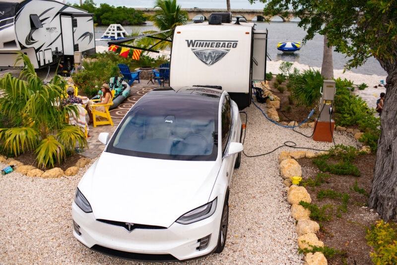 a white tesla towing a winnebago is parked at a campsite near the water