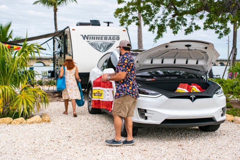 two people unpack from a white tesla at a campsite
