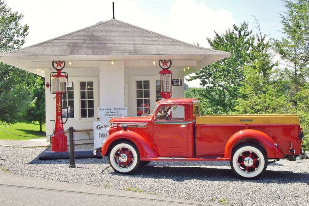 a small old gas station with two pumps and a red vintage pickup truck parked out front
