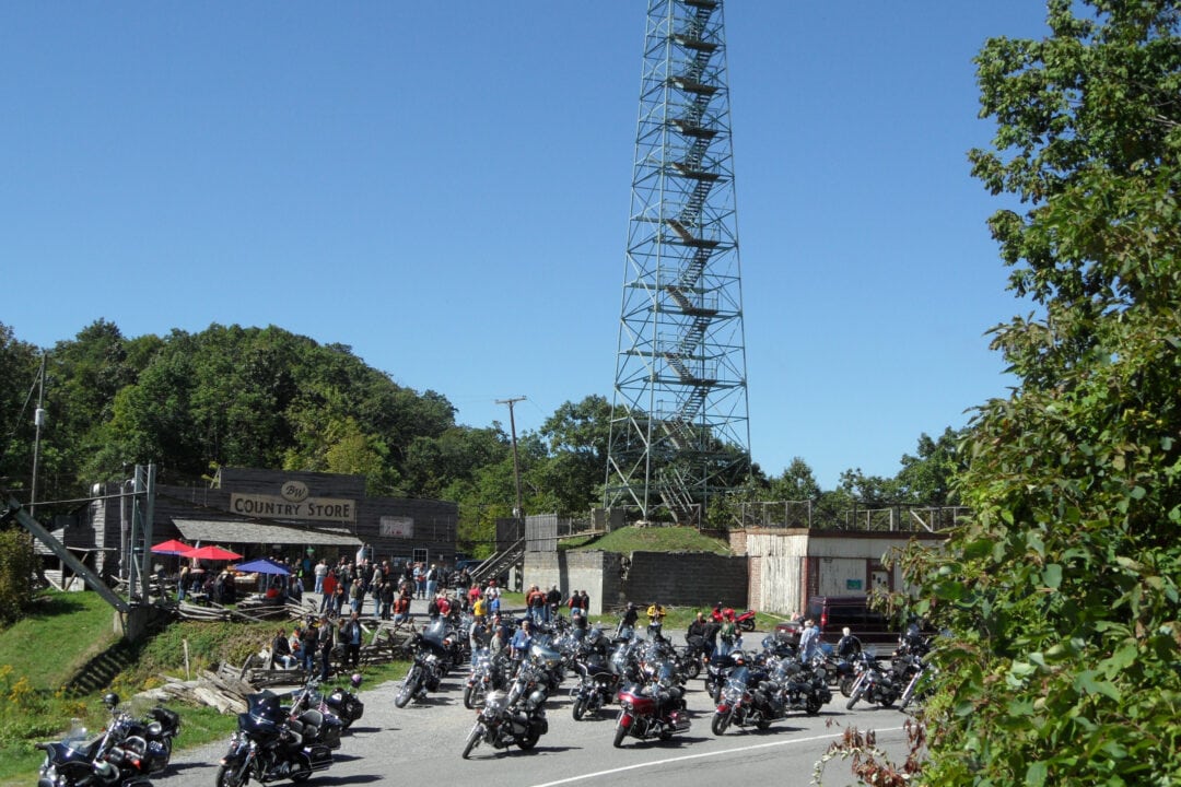 dozens of motorcycles are parked at the base of a tall lookout tower in front of a country store