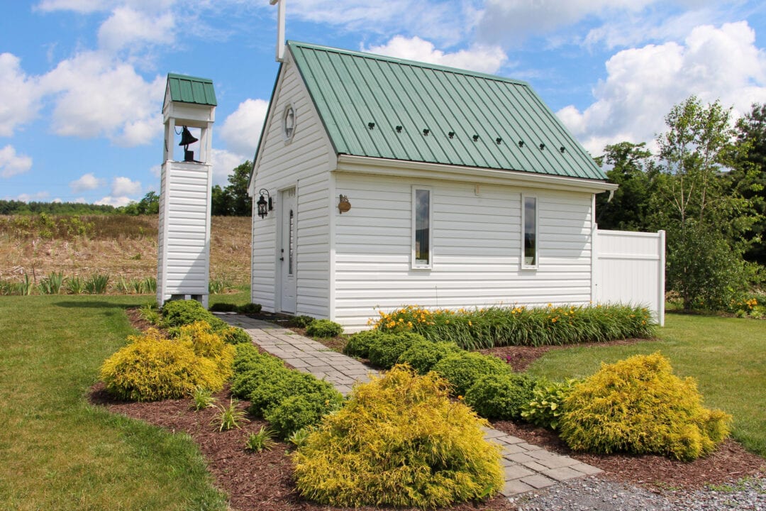 a small white church with a green roof and a bell out front