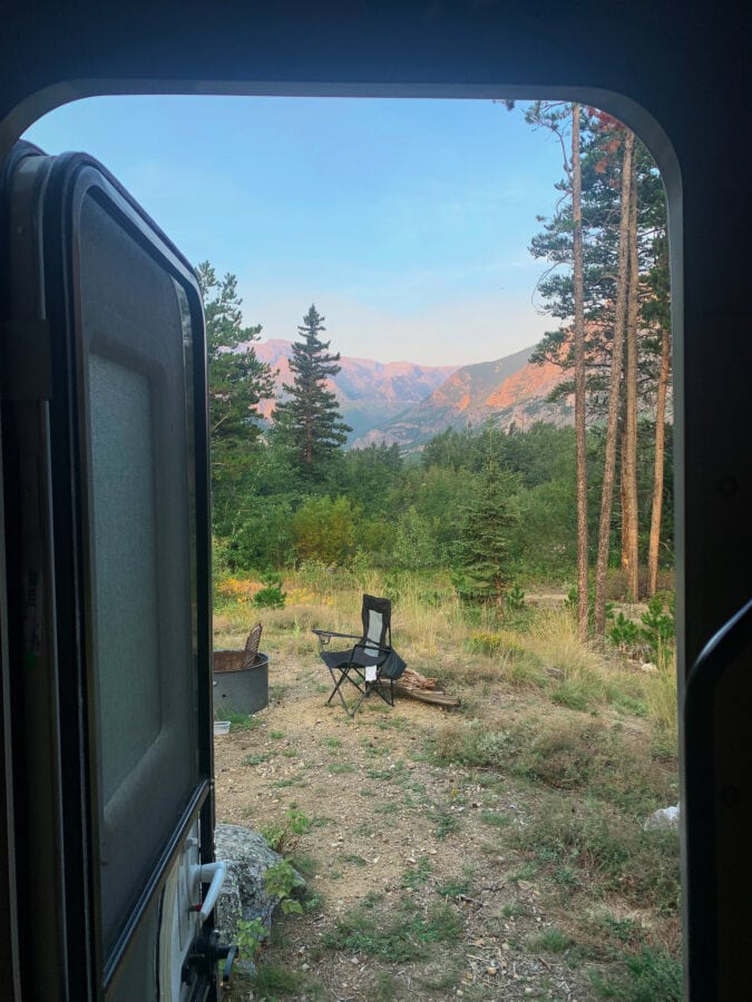 Open door of RV looking at scenic views and camp chair set up at fire pit