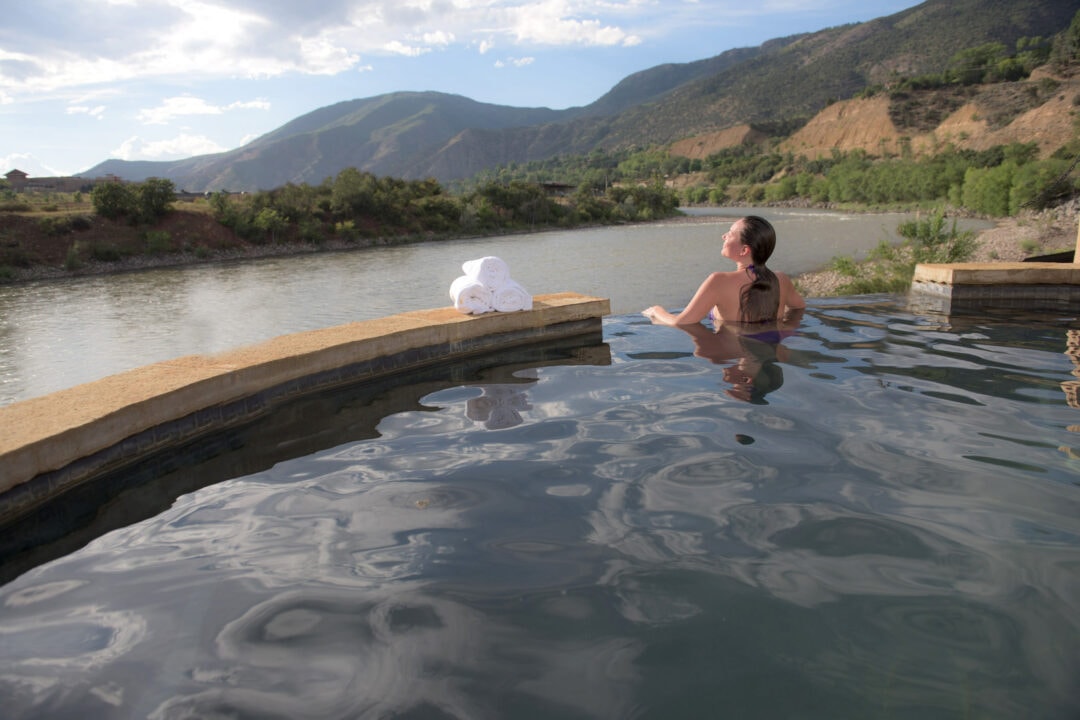 a person soaks in a hot springs pool overlooking the mountains