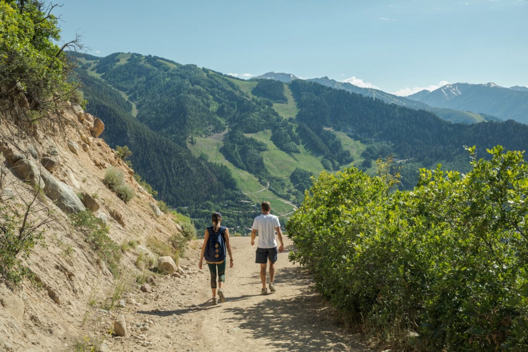 two people hike a trail in the mountains