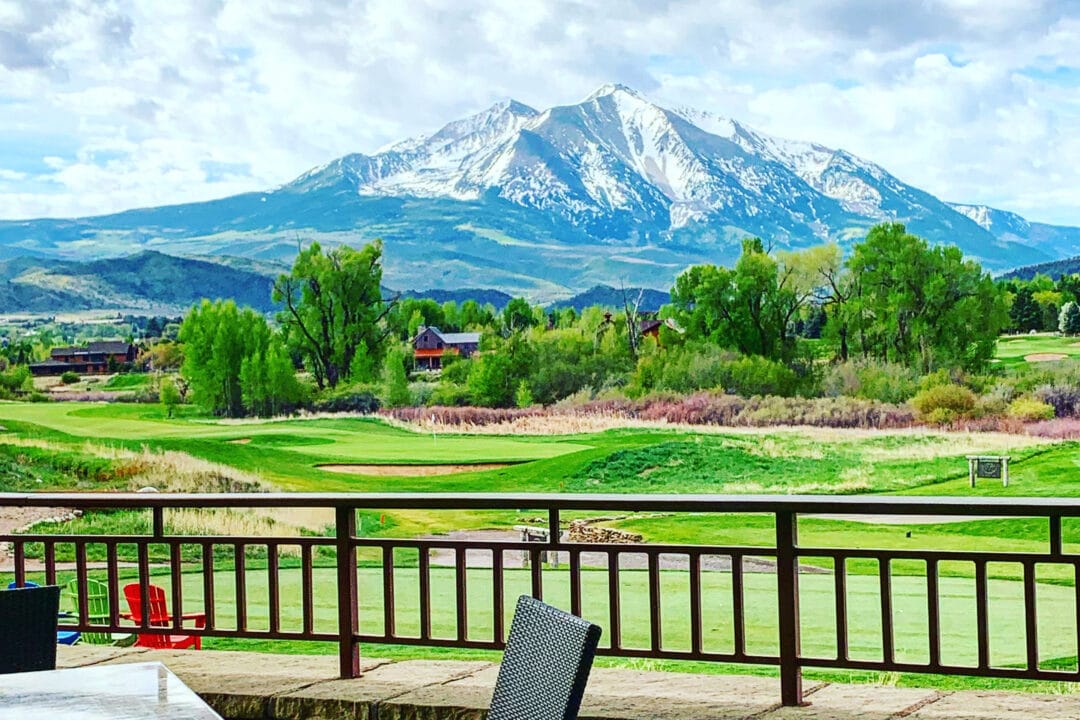 a snowy mountain peak as seen from the patio of a restaurant overlooking a golf course