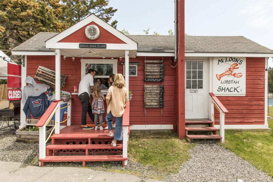 a family orders at a walk-up window of a small red and white lobster shack
