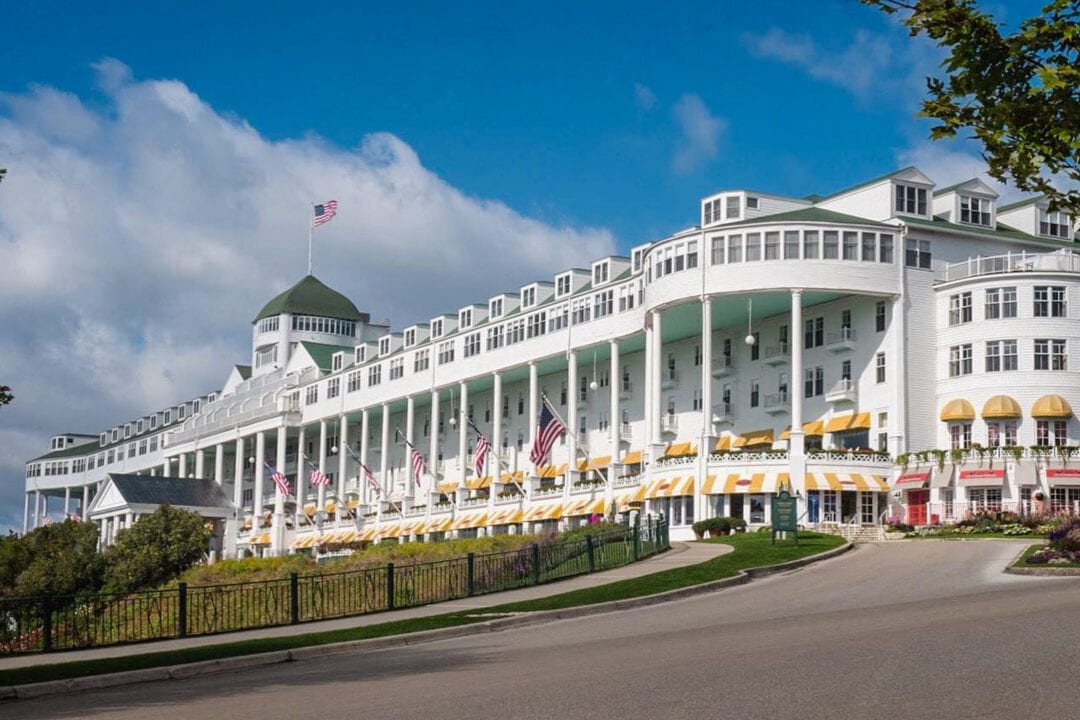 a multi-story white hotel with a large wraparound porch and yellow striped awnings