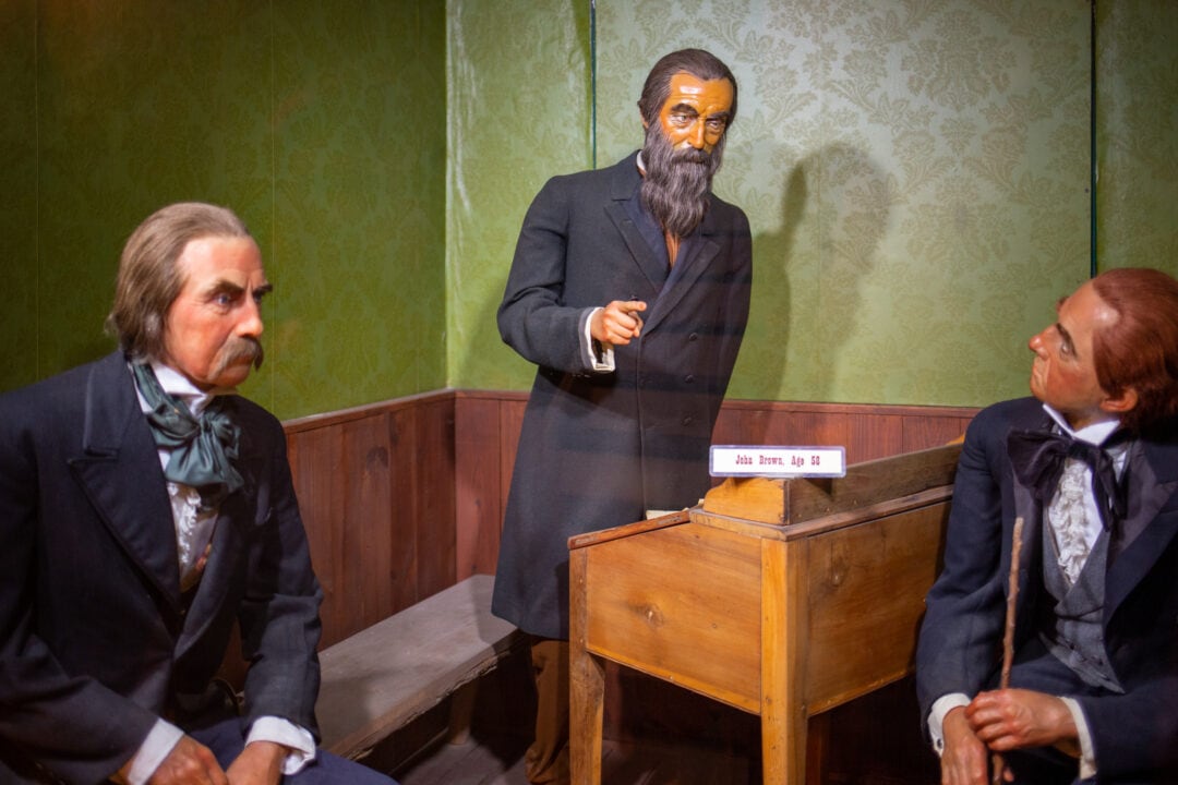 three wax figures in suits, two are seated and one is standing at a wooden lecturn