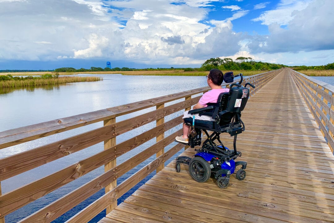 a wheelchair user is on a wooden boardwalk over the water