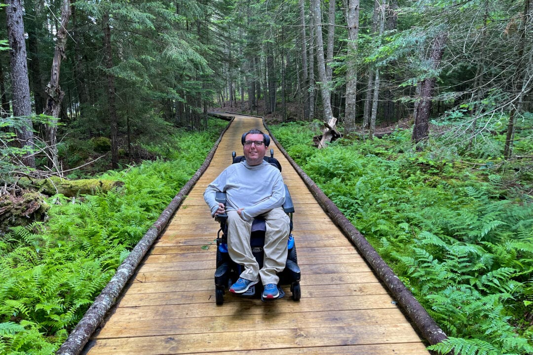 a wheelchair user on a wooden boardwalk through the woods