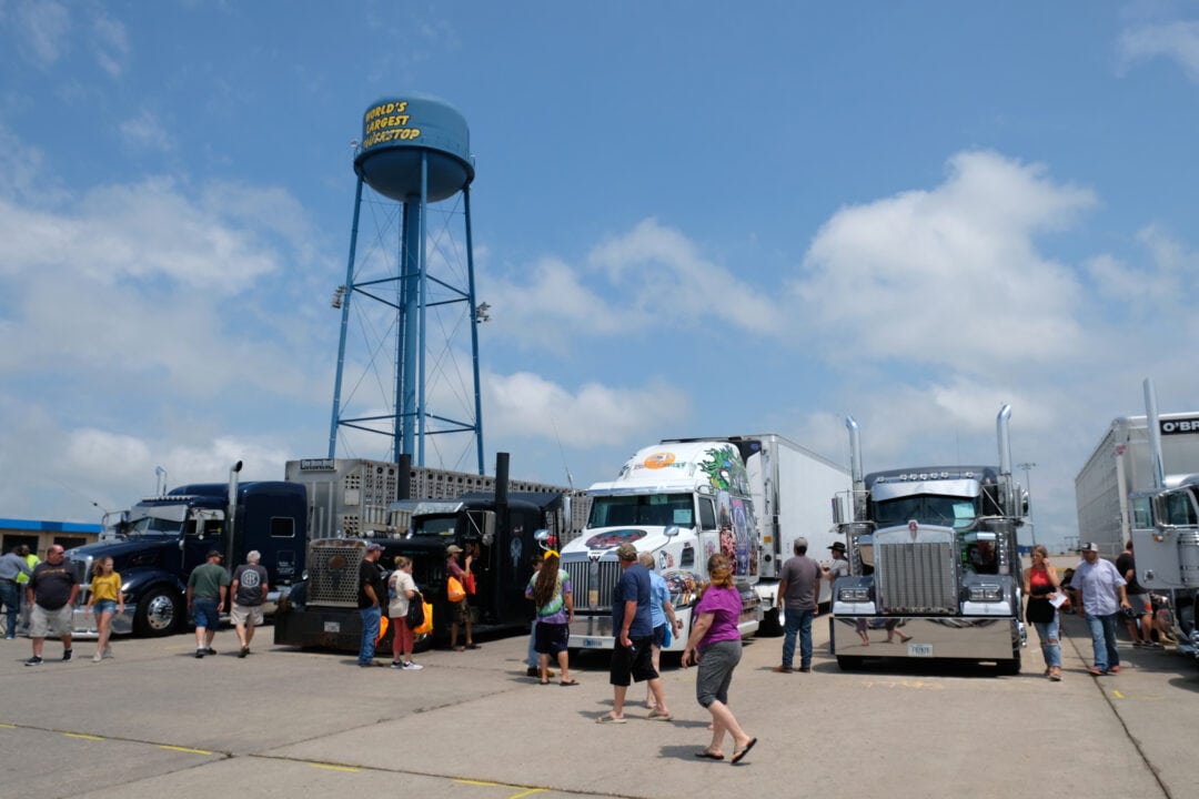 people walk under a water tower in a parking lot full of large trucks