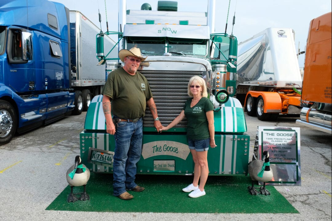 two people hold hands and stand in front of a truck cab named "the goose"