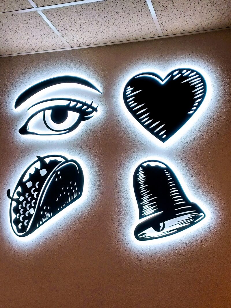 four black illustrations of an eye, a heart, a taco and a bell surrounded by a white glow on a white wall