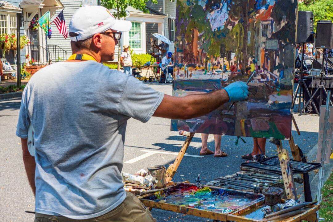 a man paints at an easel outside on a lively street