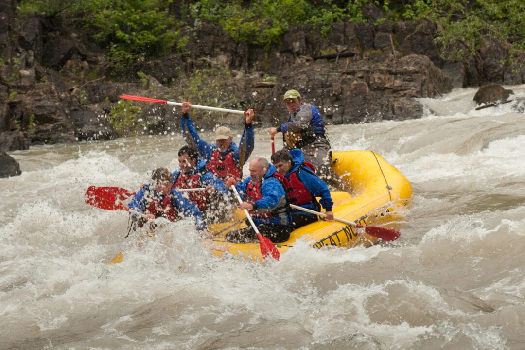 six people in a yellow raft fight whitewater rapids