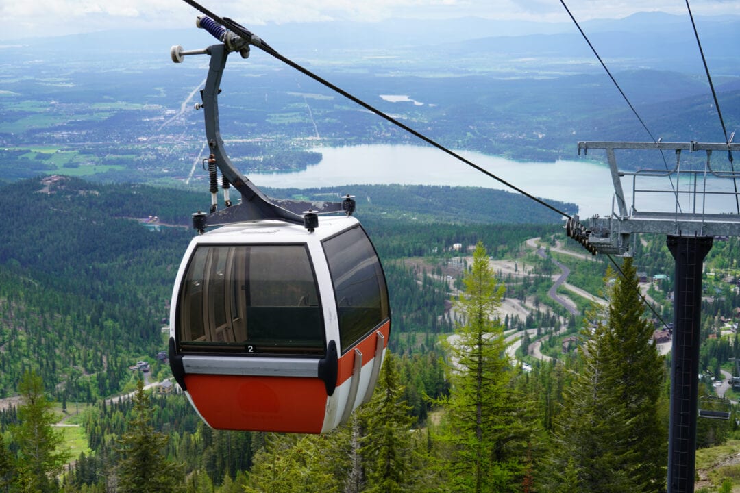 a red and white gondola on a track high above pine trees