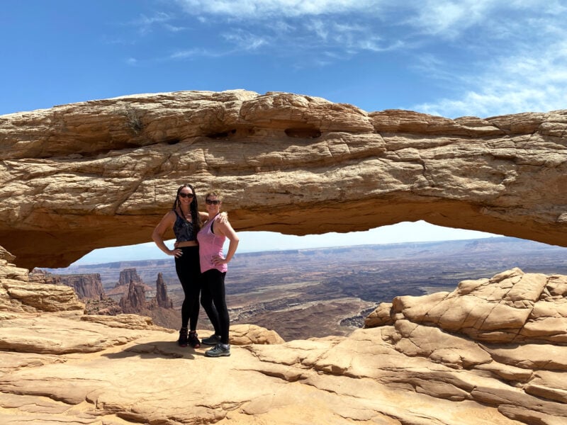 two people pose in front of a sandstone arch