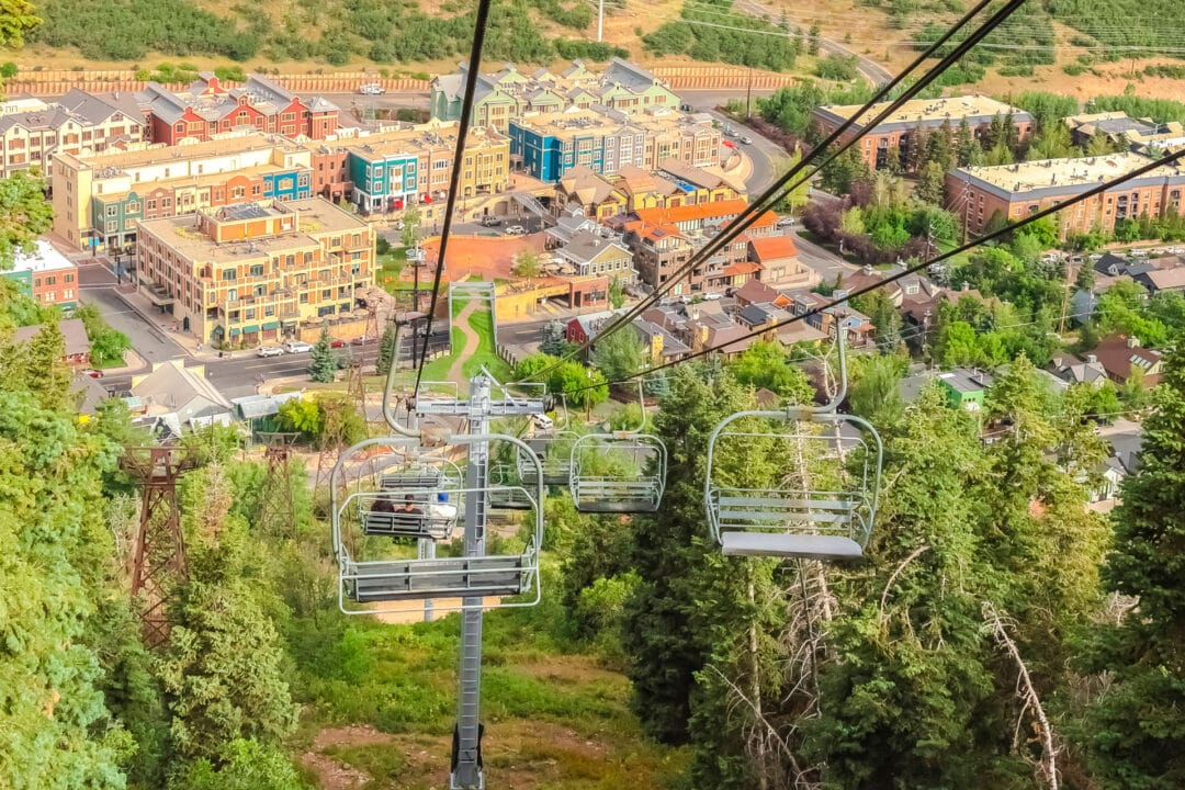 Panorama view of empty chairlifts over a city and green trees
