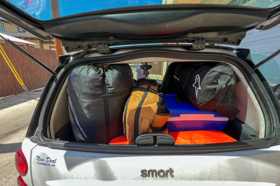 a white smart car with the trunk open packed with camping gear