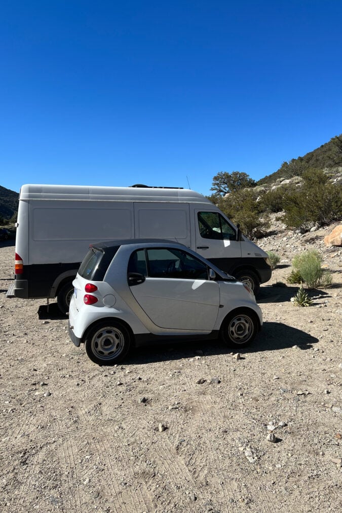 a small white smart car parked next to a large white campervan
