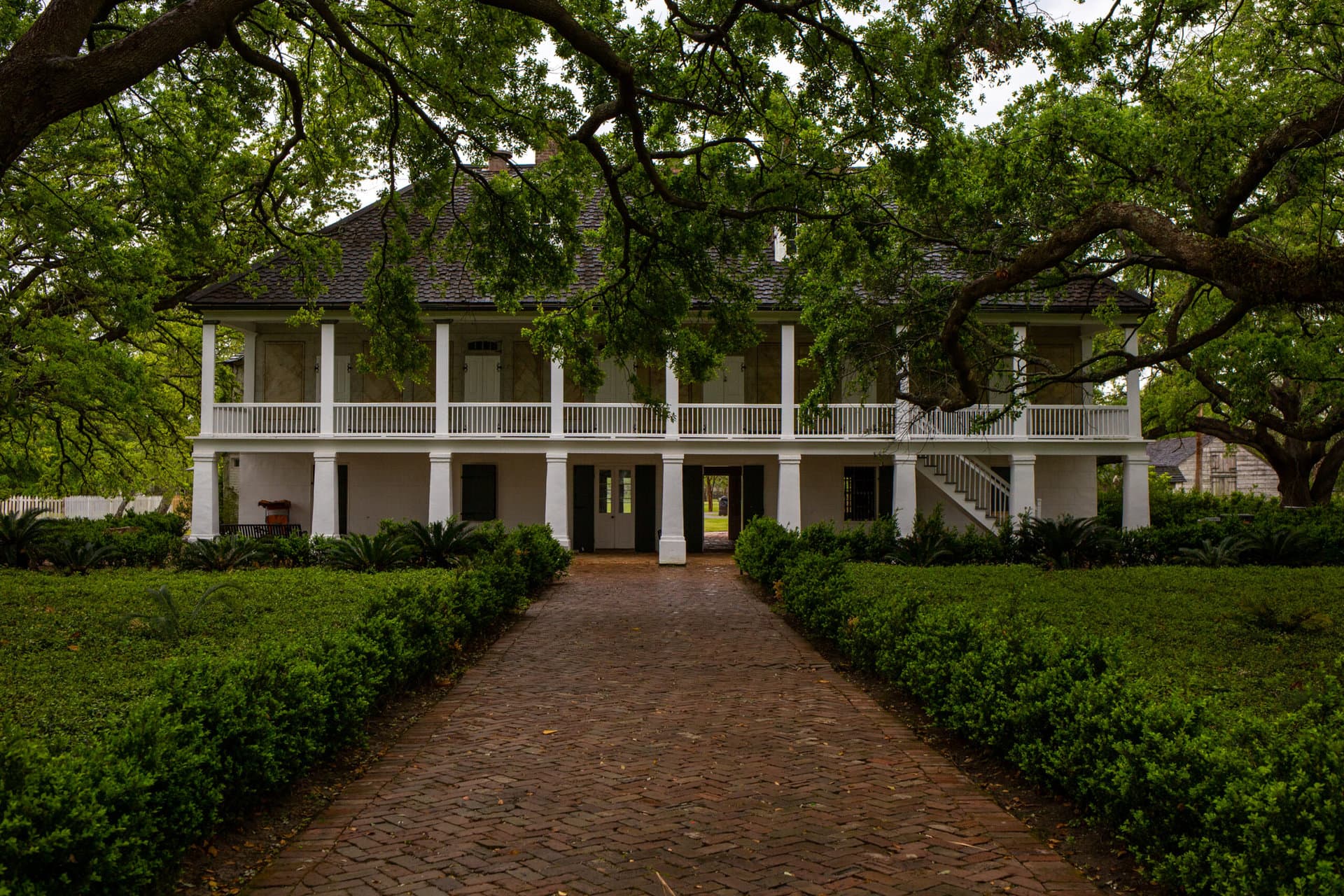 a 3-story white house with a large porch and columns surrounded by trees and a brick path