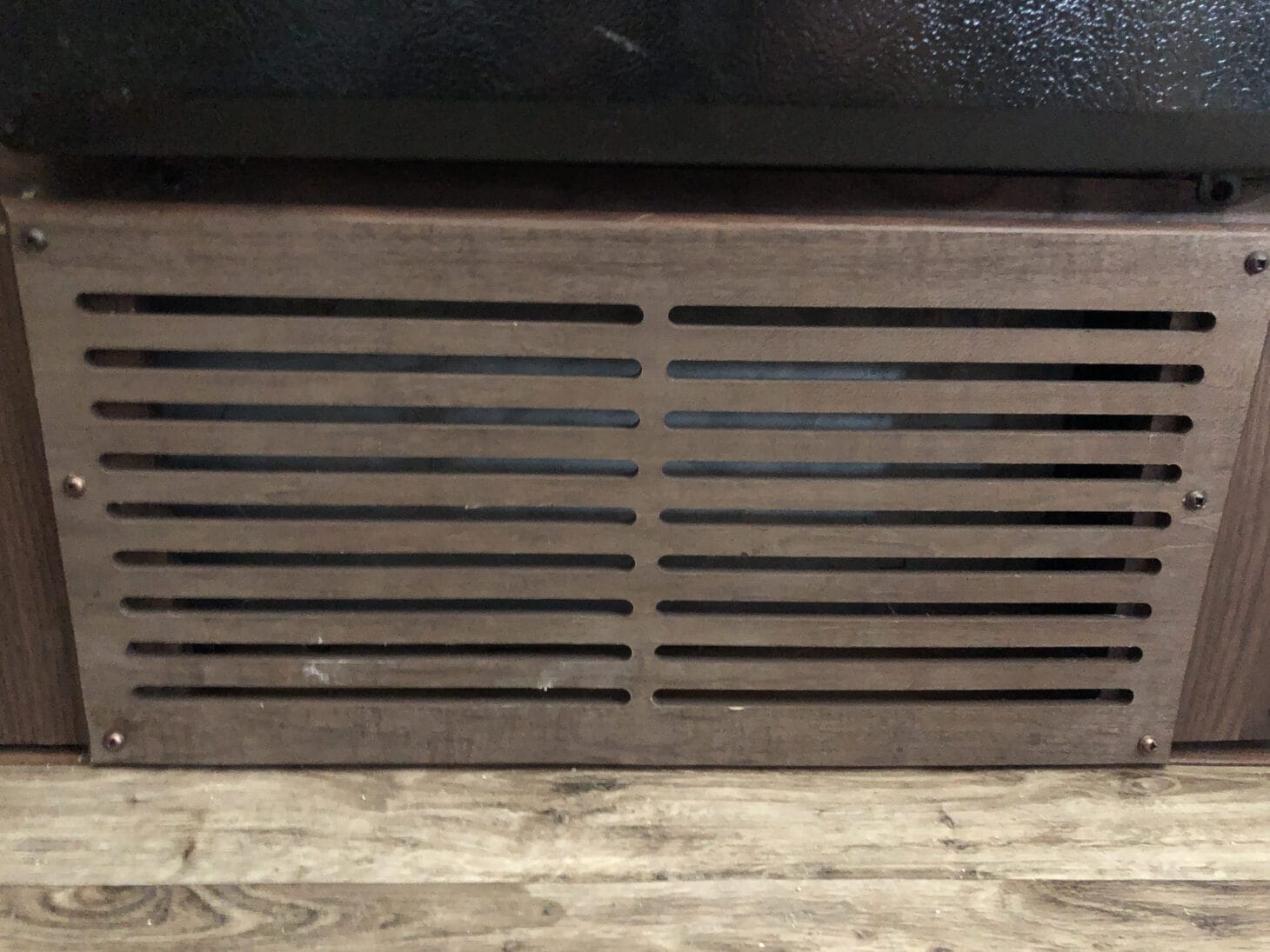 Wooden cover over a furnace return vent under bench seating in an RV
