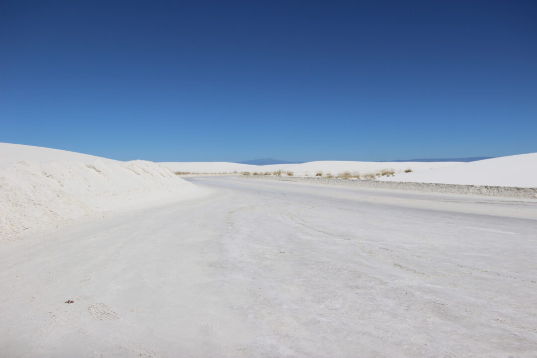 a large flat expanse of white surrounded by white dunes under a clear blue sky