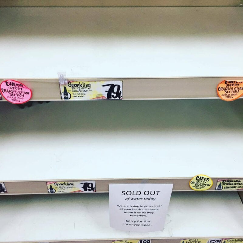 Empty shelves at a grocery store with sign about hurricane preparedness