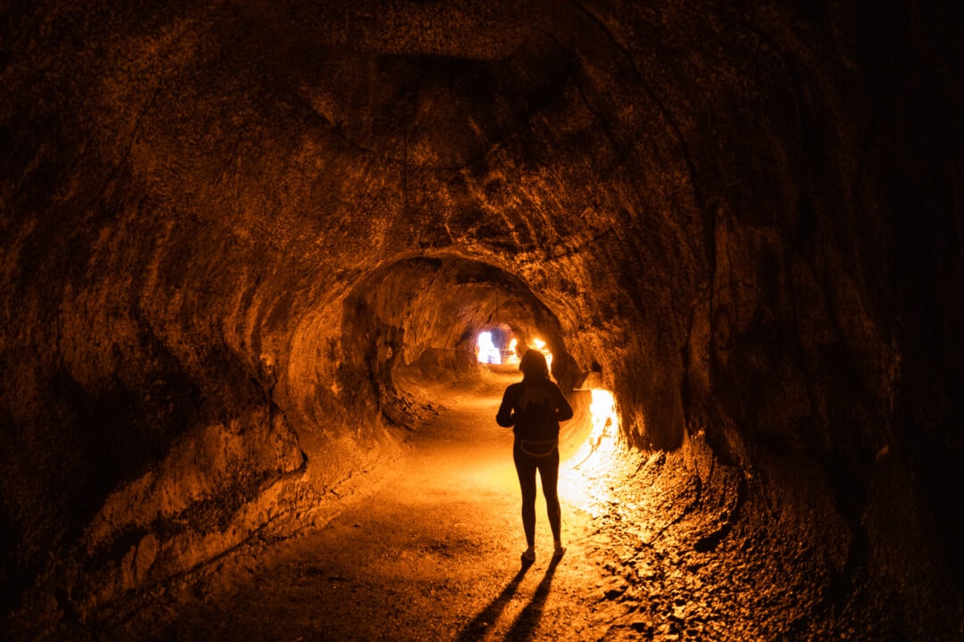 a person stands in a tunnel carved into rock and lit by an orange glow