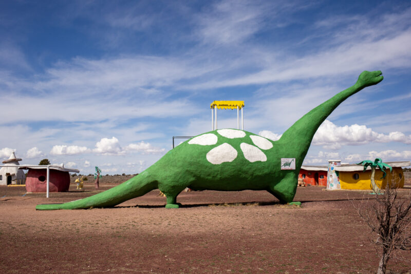 a green concrete dinosaur slide set against a blue sky with wispy white clouds